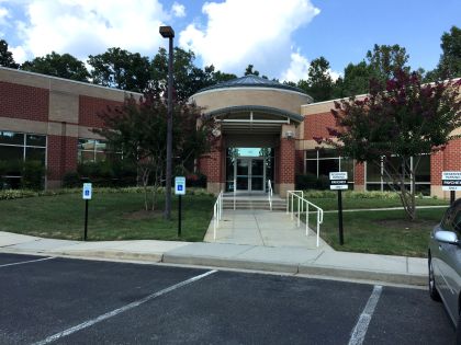 Modern building entrance with landscaped grounds, featuring steps and a ramp. Signage indicates accessible parking. Ideal for community services.
