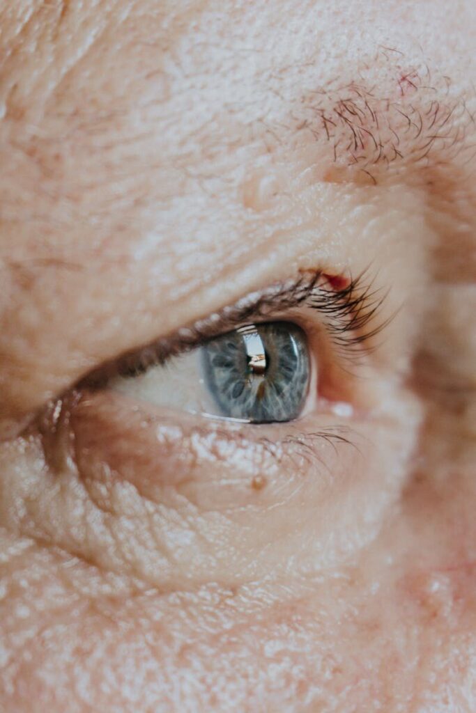 Close-up view of an elderly person's blue eye, capturing details of the skin and eyelashes.